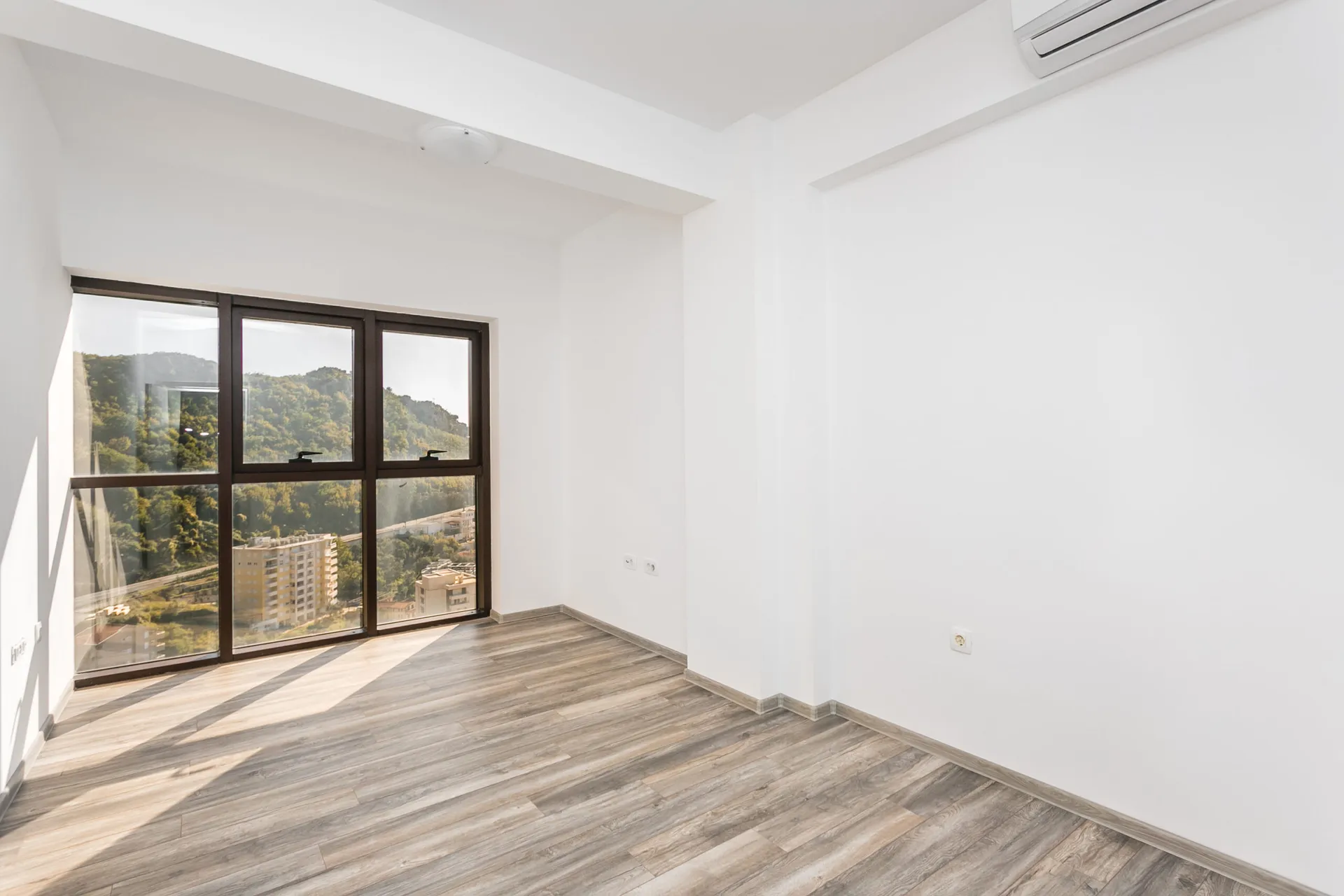 Helles Wohnzimmer im Penthouse in Rafailovići, Montenegro: Panoramafenster mit Bergblick, Laminatboden und weiße Wände.