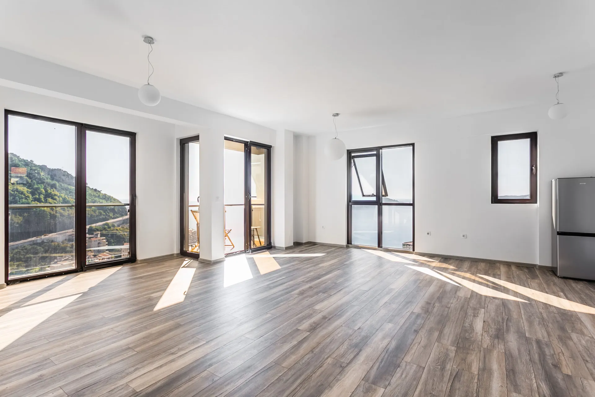 Helles Wohnzimmer im Penthouse in Rafailovići, Montenegro, mit Panoramafenstern, Meer- und Bergblick und Holzoptik-Boden.
