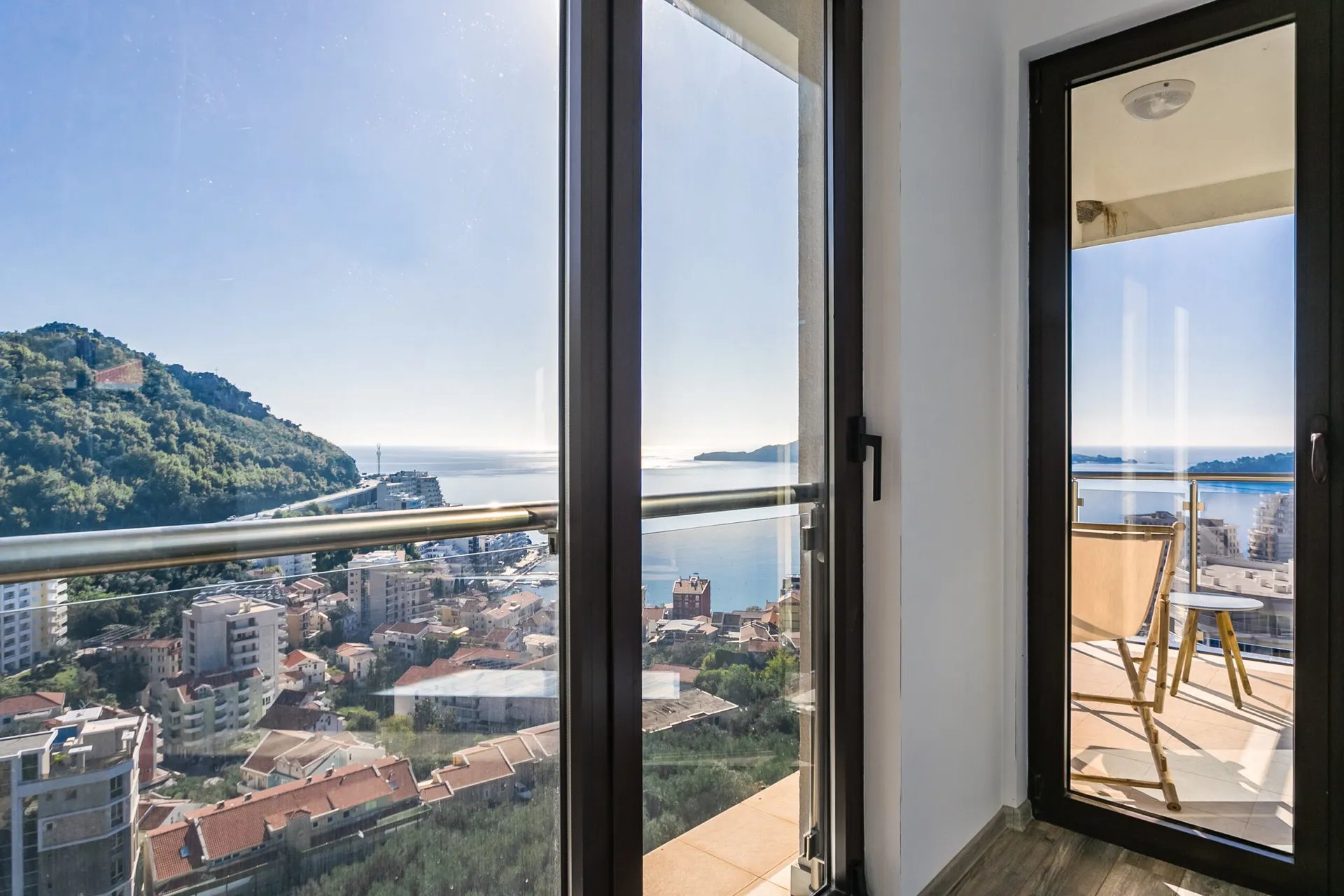 Blick vom Balkon des Penthouses in Rafailovići, Montenegro: Panorama von Meer, Bergen und Stadt durch eine Glasbrüstung.