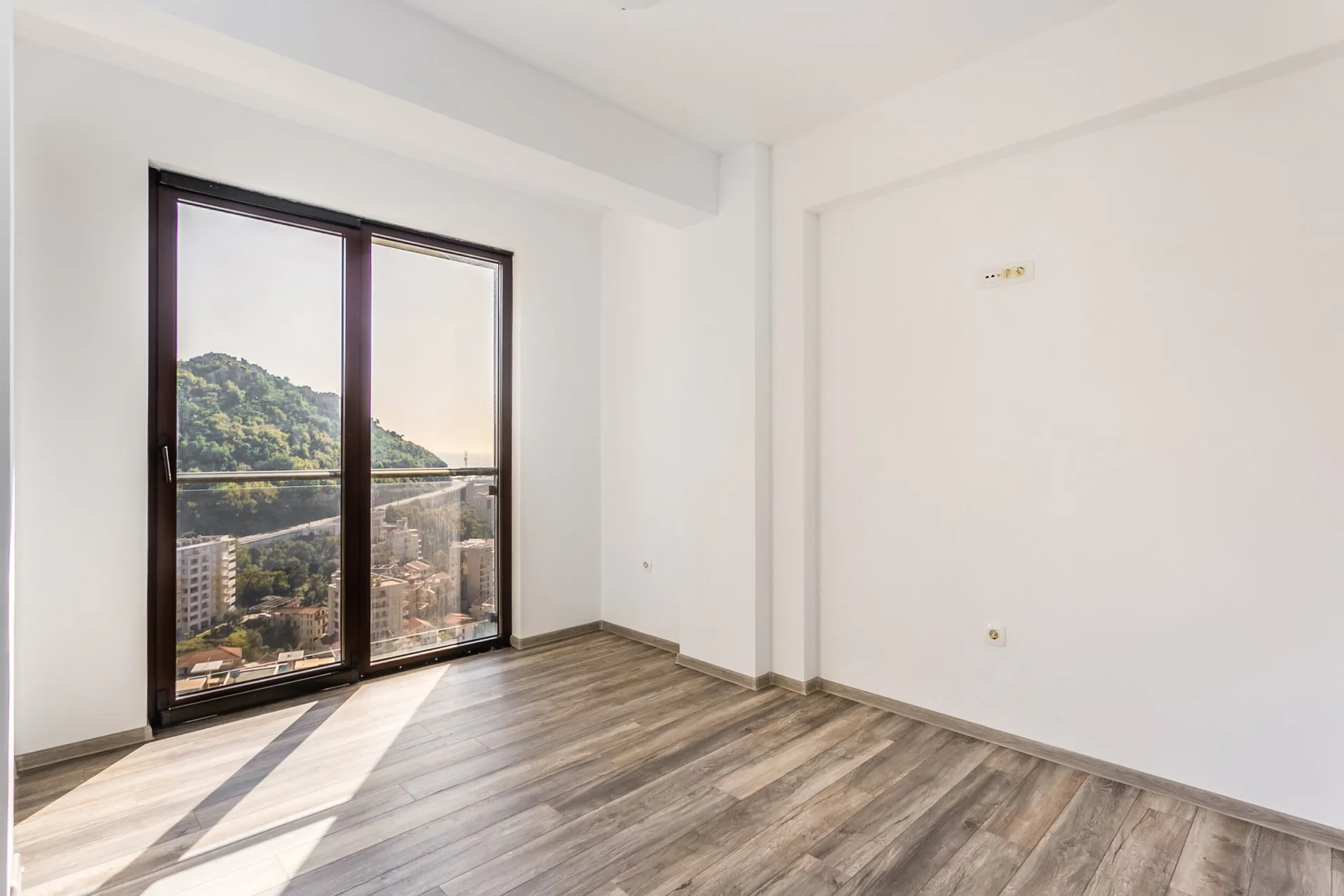Helles Wohnzimmer im Penthouse in Rafailovici, Montenegro: Panoramafenster mit Bergblick, Laminatboden und weiße Wände.