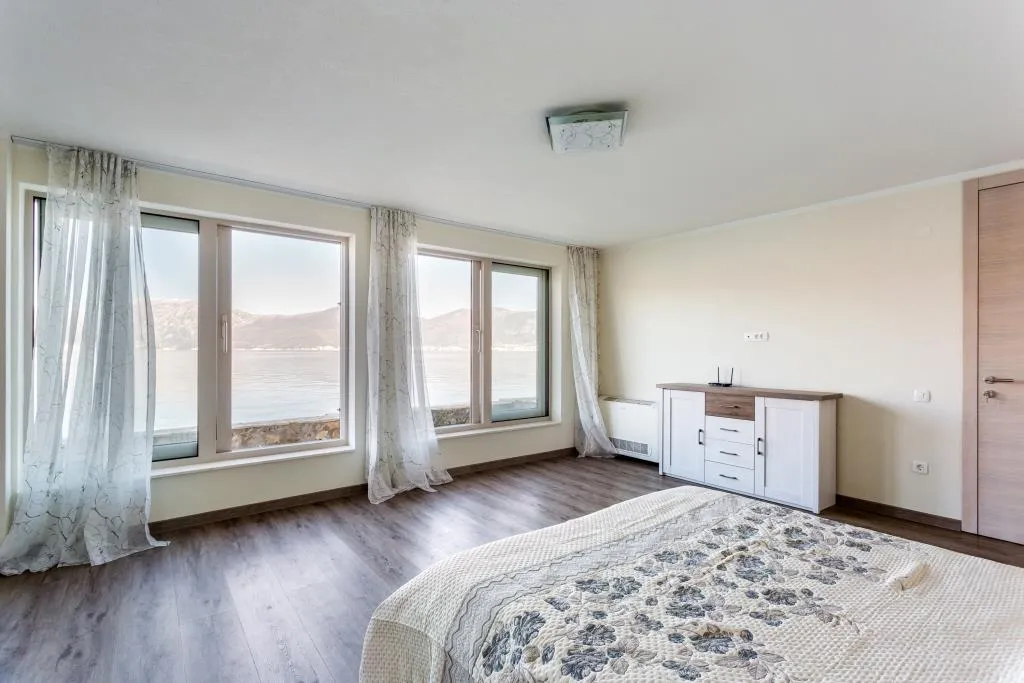 Bedroom with panoramic sea view in a villa, Krašići, Montenegro: bright interior, double bed, and dresser.