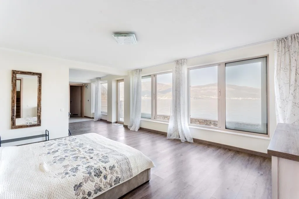 Bedroom with panoramic sea and mountain views in a villa, Krašići, Montenegro: bright interior, double bed, and mirror.