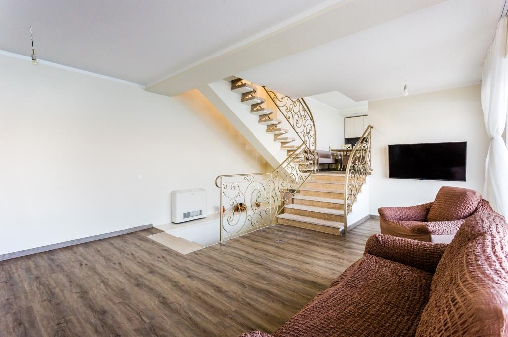 Living room with a wrought-iron staircase in a villa, Krašići, Montenegro: bright interior, soft furniture, and laminate flooring.