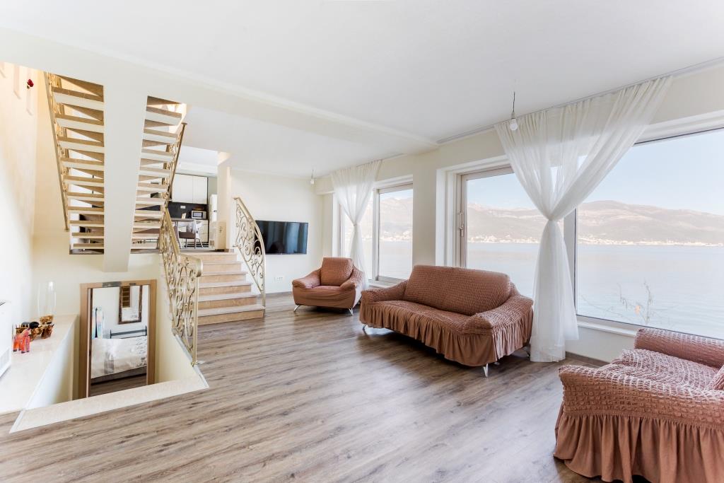 Living room in a villa in Krašići, Montenegro: panoramic sea view, soft seating, staircase, and modern interior.