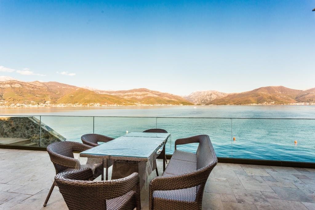 Villa terrace in Krašići, Montenegro: wicker furniture, glass railing, and panoramic sea and mountain views.
