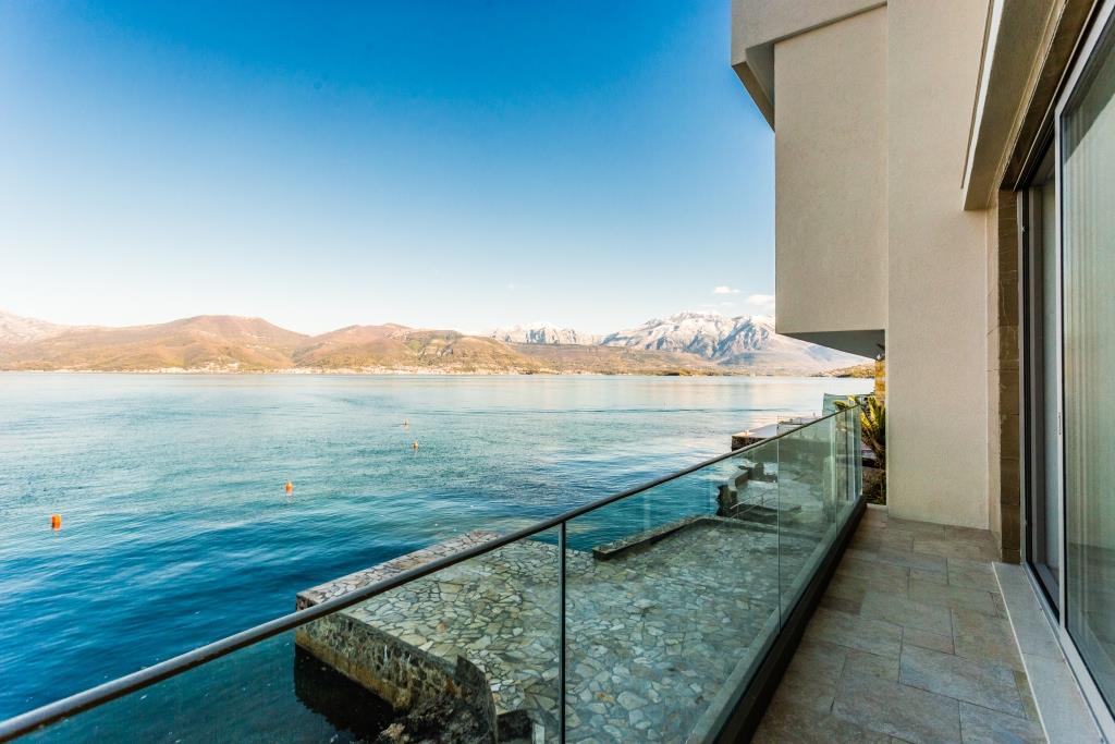 Villa balcony in Krašići, Montenegro: panoramic sea and mountain view, glass railing, stone floor finish.
