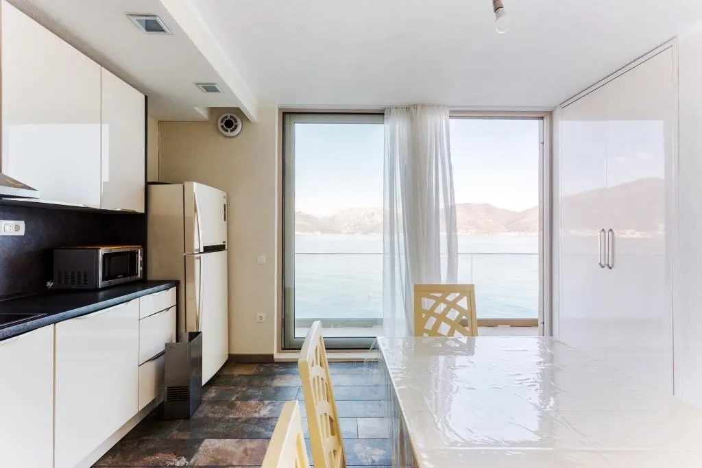 Modern kitchen with sea view in a villa, Krašići, Montenegro: white furniture, dining area, and panoramic windows.