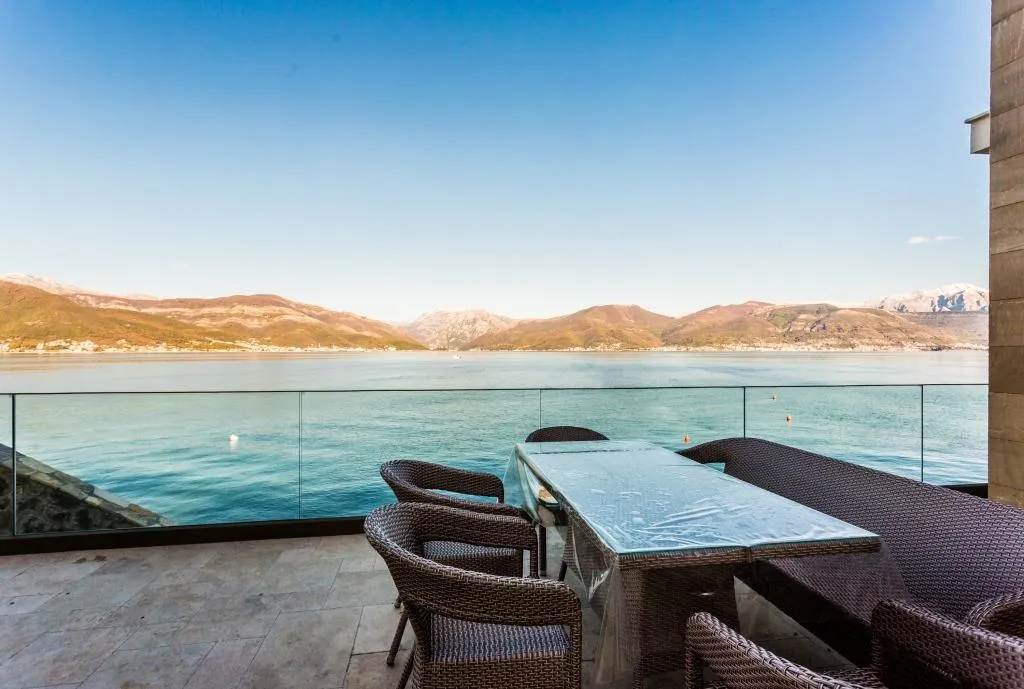 Villa terrace in Krašići, Montenegro: wicker furniture, glass railing, and panoramic sea and mountain views.