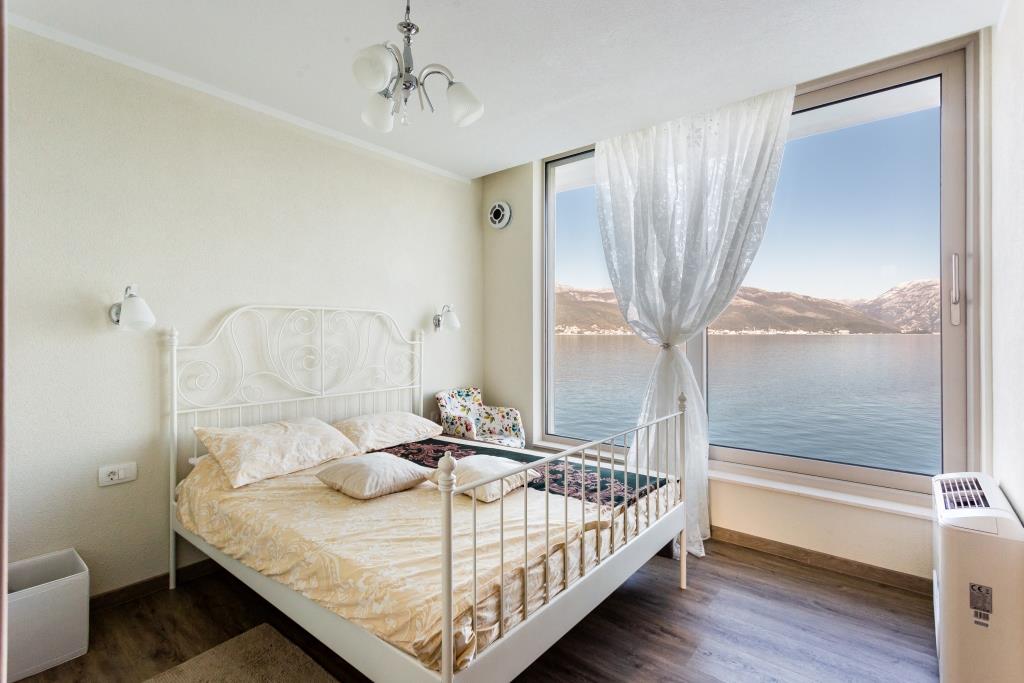 Bedroom with panoramic sea and mountain views in a villa, Krasici, Montenegro: white wrought-iron bed and bright interior.