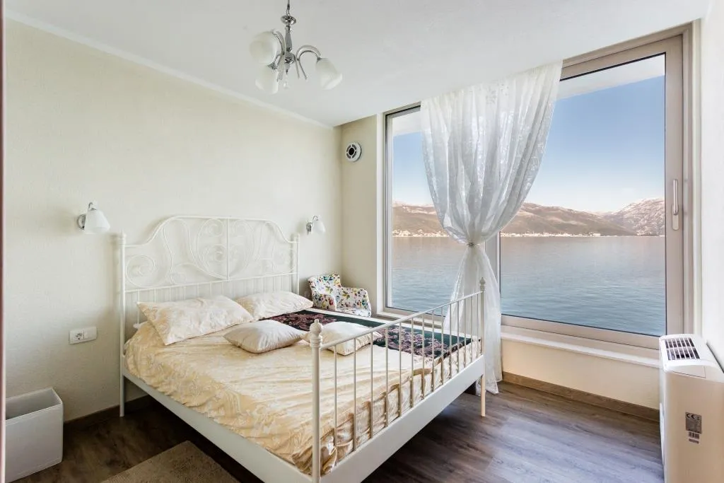 Bedroom with panoramic sea and mountain views in a villa, Krasici, Montenegro: white wrought-iron bed and bright interior.