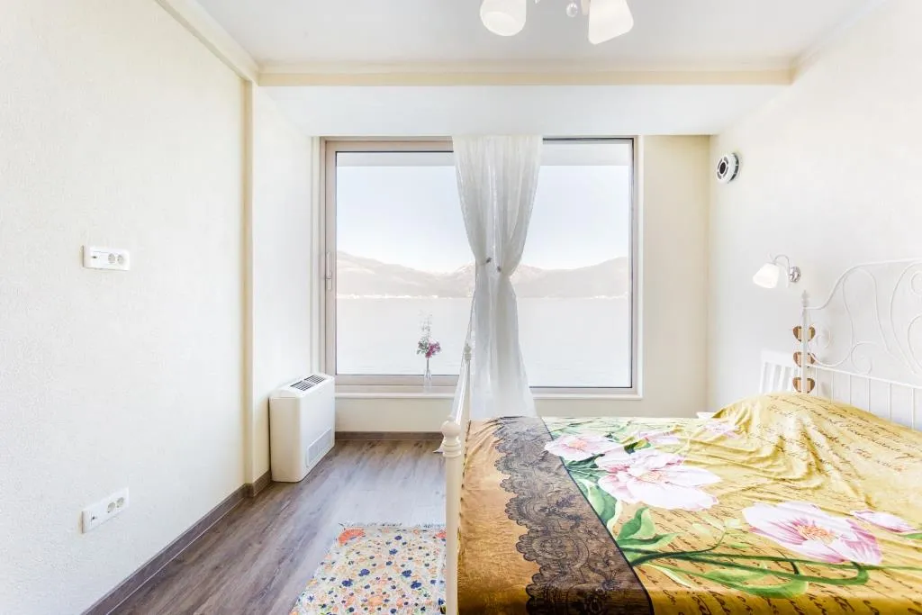 Bright bedroom with sea view in a villa, Krašići, Montenegro: double bed, panoramic window, and laminate flooring.