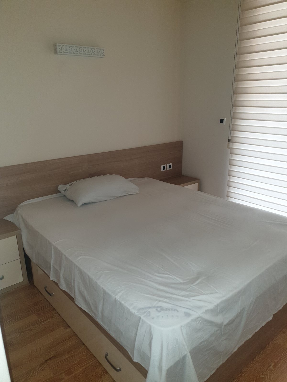 Helles Schlafzimmer mit Doppelbett und Holz-Kopfteil in einer Wohnung, Stadt Budva, Montenegro.