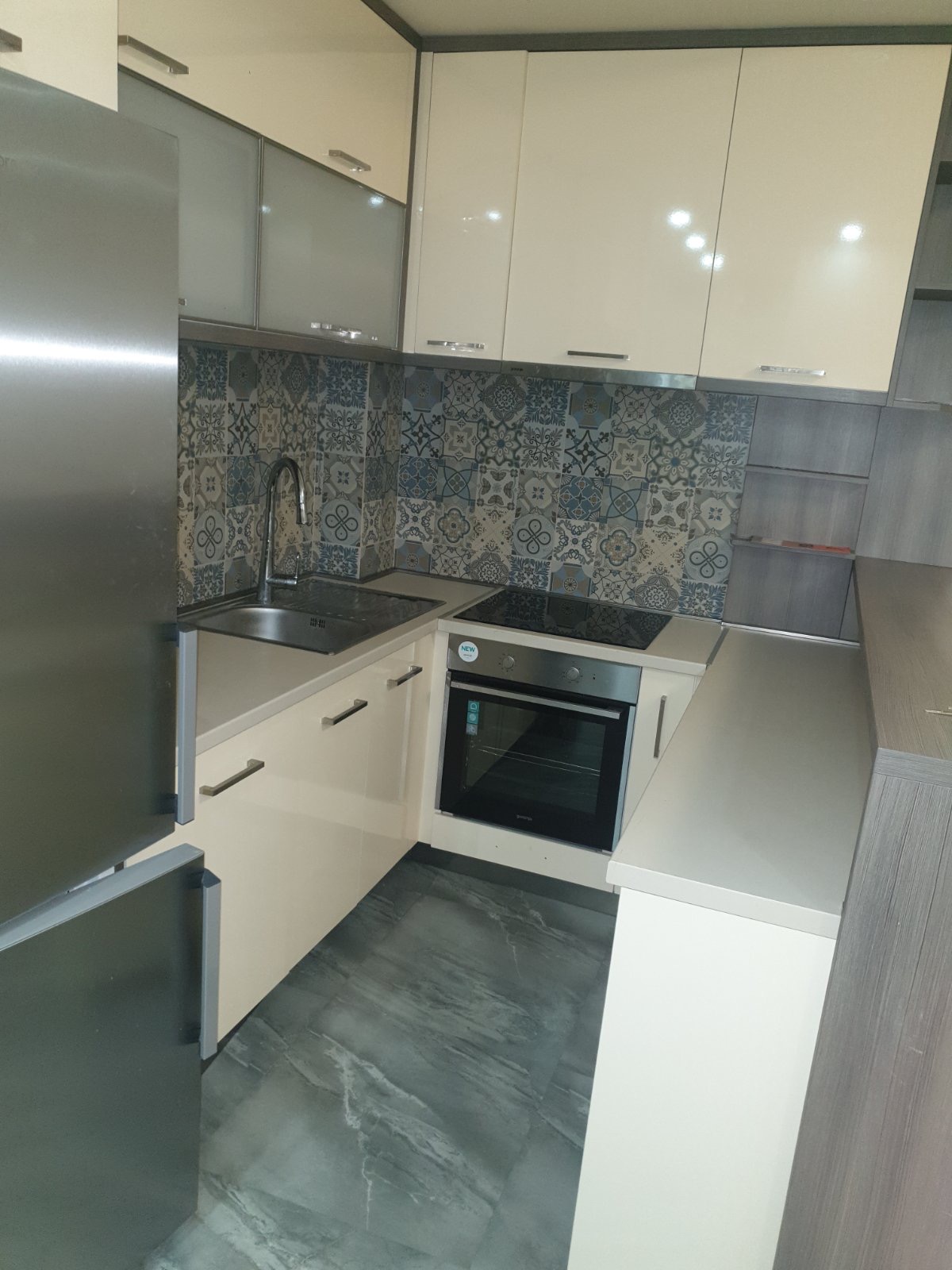 Moderne Küche in einer Wohnung in Budva, Montenegro: helle Einbauküche, gemusterter Fliesenspiegel und integrierte Haushaltsgeräte.