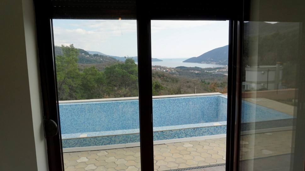 Vue depuis la fenêtre de la villa à Igalo, Monténégro : piscine en mosaïque, terrasse et vue panoramique sur la mer et les montagnes.