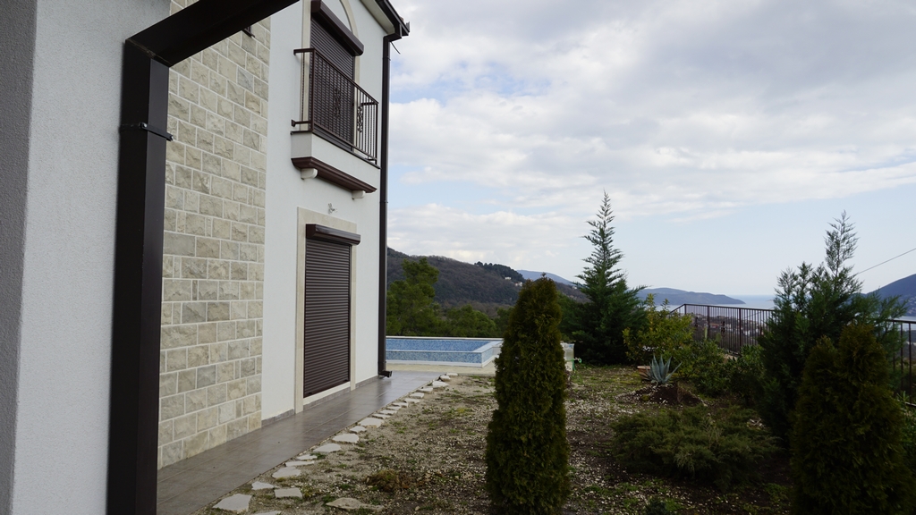 Façade de la villa à Igalo, Monténégro : parement en pierre, piscine, jardin et vue panoramique sur la mer et les montagnes.