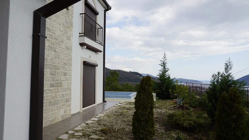 Façade de la villa à Igalo, Monténégro : parement en pierre, piscine, jardin et vue panoramique sur la mer et les montagnes.