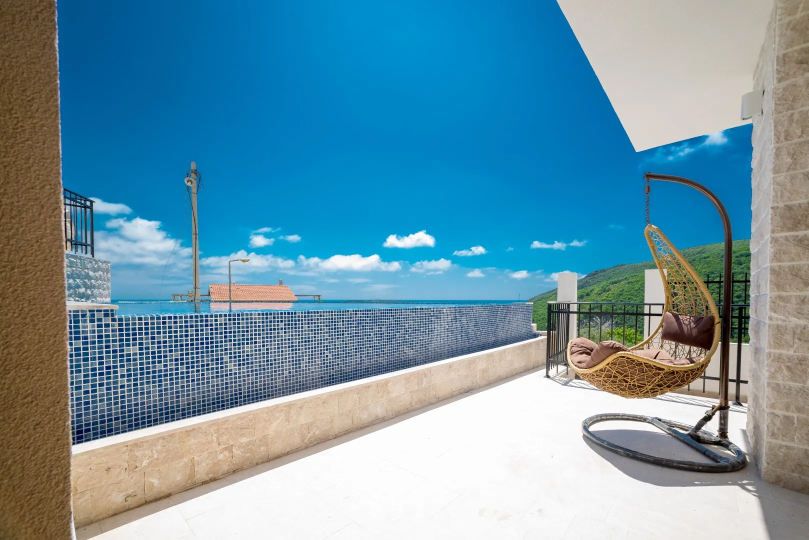 Balkon mit Hängestuhl, Swimmingpool und Meerblick.