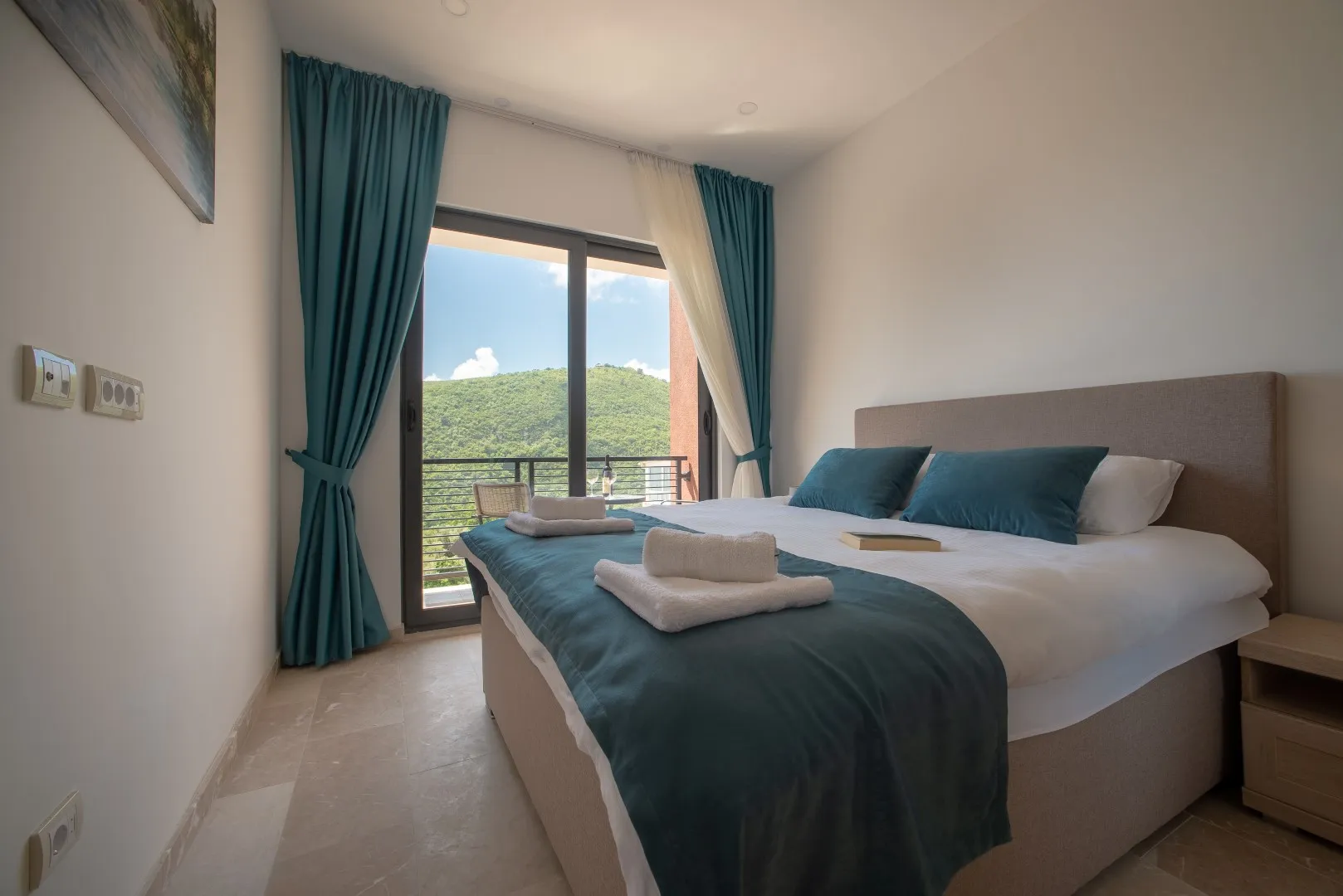 Schlafzimmer mit Doppelbett, blauen Kissen, Decke und Balkonblick.