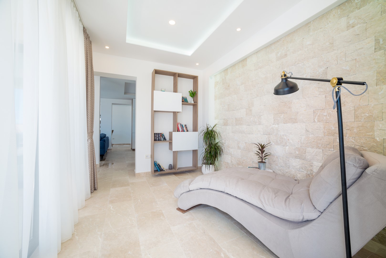 Wohnzimmer in einer Villa in Bečići, Montenegro: Liegestuhl, Regal und Akzentwand aus Naturstein im Interieur.