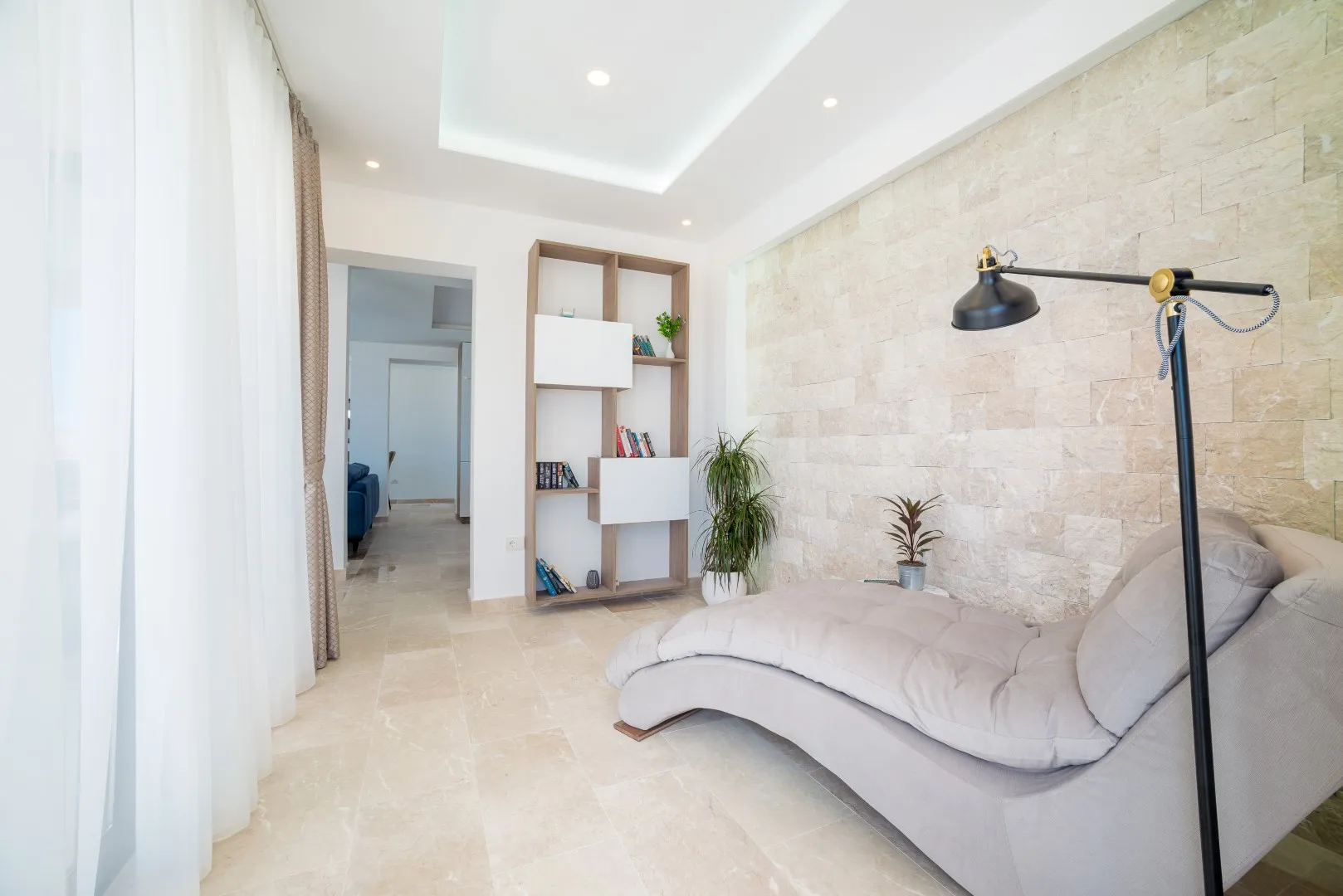 Geräumiges, helles Wohnzimmer mit beigem Liegestuhl und Steinwand