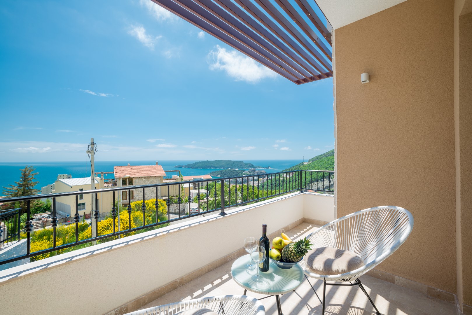 Balkon der Villa in Bečići, Montenegro: Panoramablick auf das Meer, Rattanmöbel, Tisch mit Wein und Früchten.