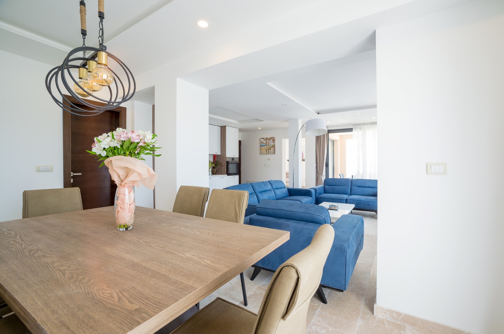 Modernes Wohnzimmer mit Essbereich in einer Villa in Bečići, Montenegro: Holztisch, blaue Sofas und helles Interieur.