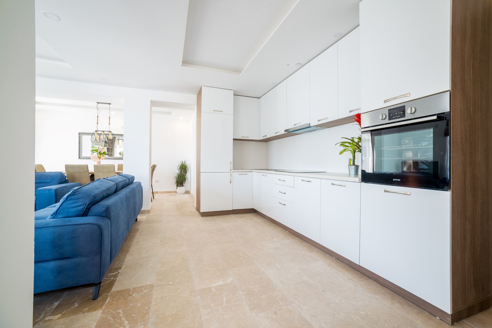 Moderne Küche mit weißen Fronten und blauem Sofa im Interieur einer Villa in Bečići, Montenegro.