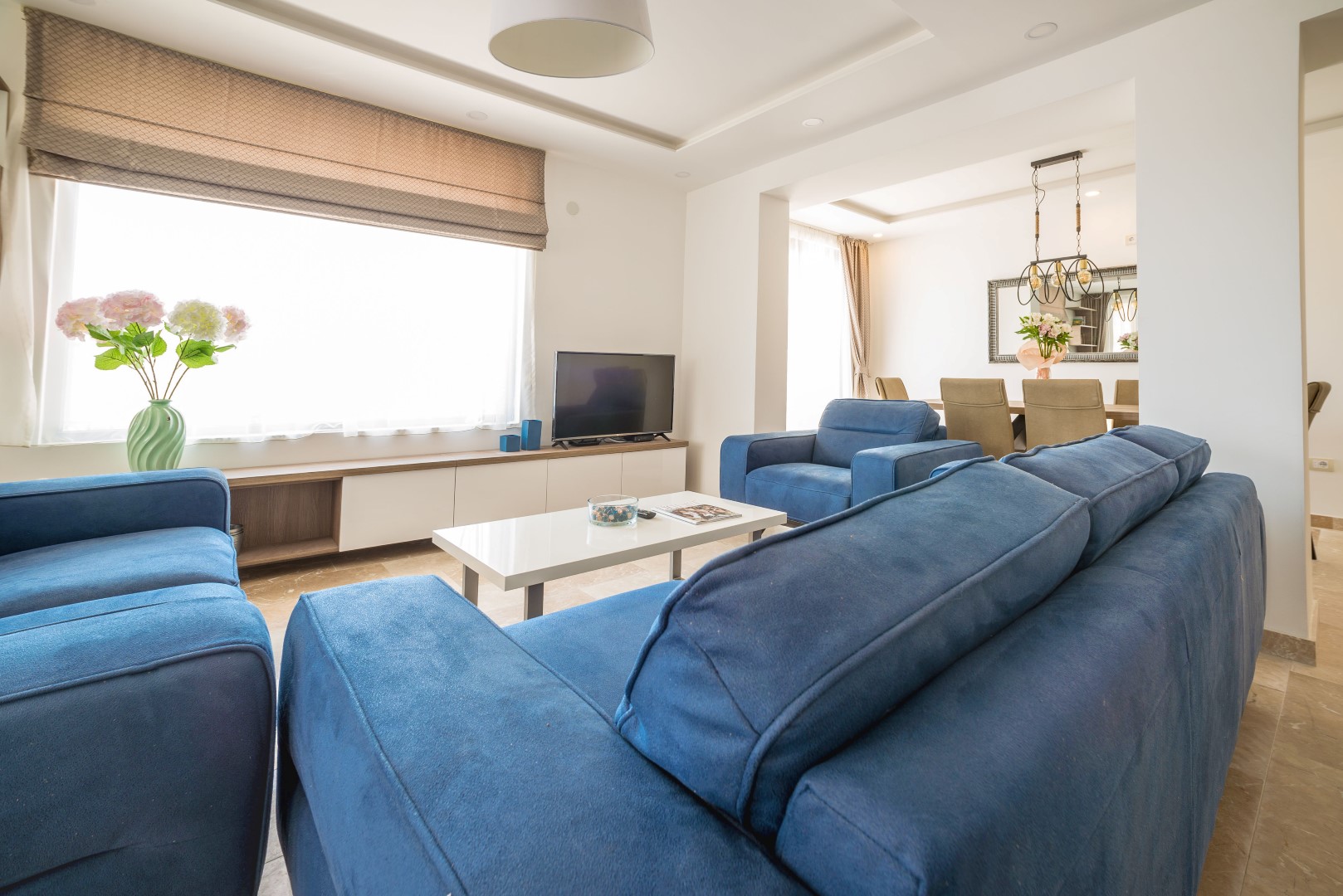 Helles Wohnzimmer mit blauen Sofas in einer Villa in Bečići, Montenegro: modernes Interieur, Essbereich und TV-Bereich.
