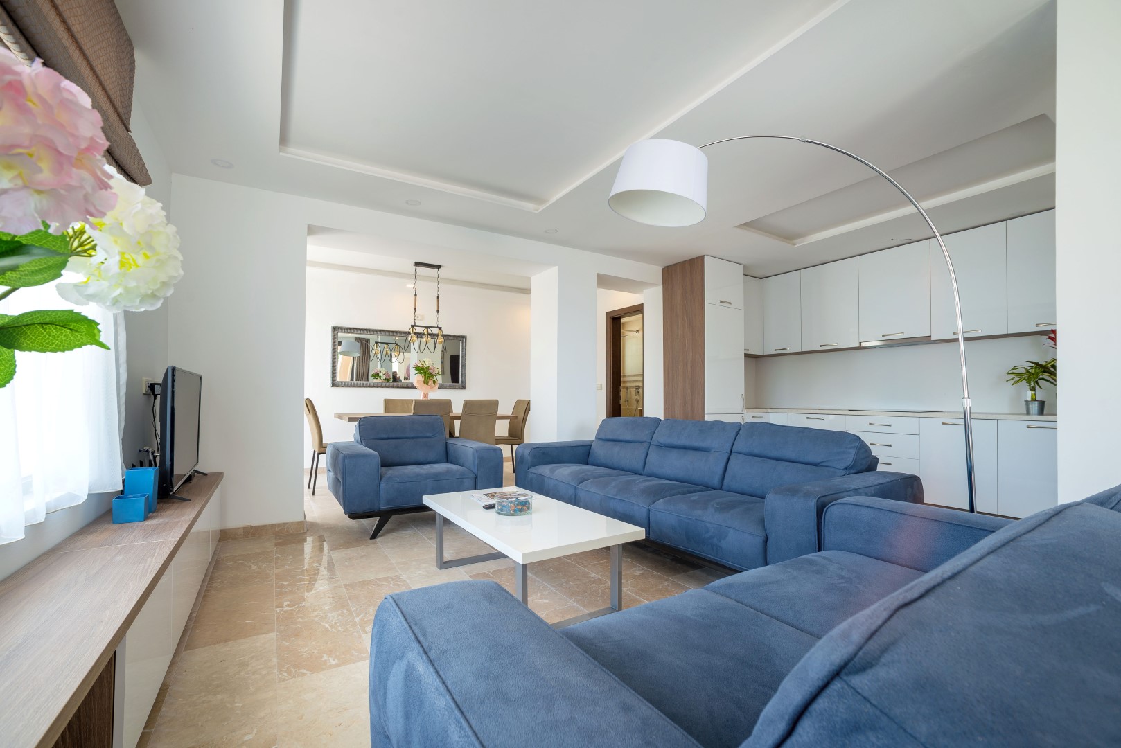 Modernes Wohnzimmer mit blauen Sofas und Küche in einer Villa in Bečići, Montenegro: Marmorboden und stilvolles Interieur.