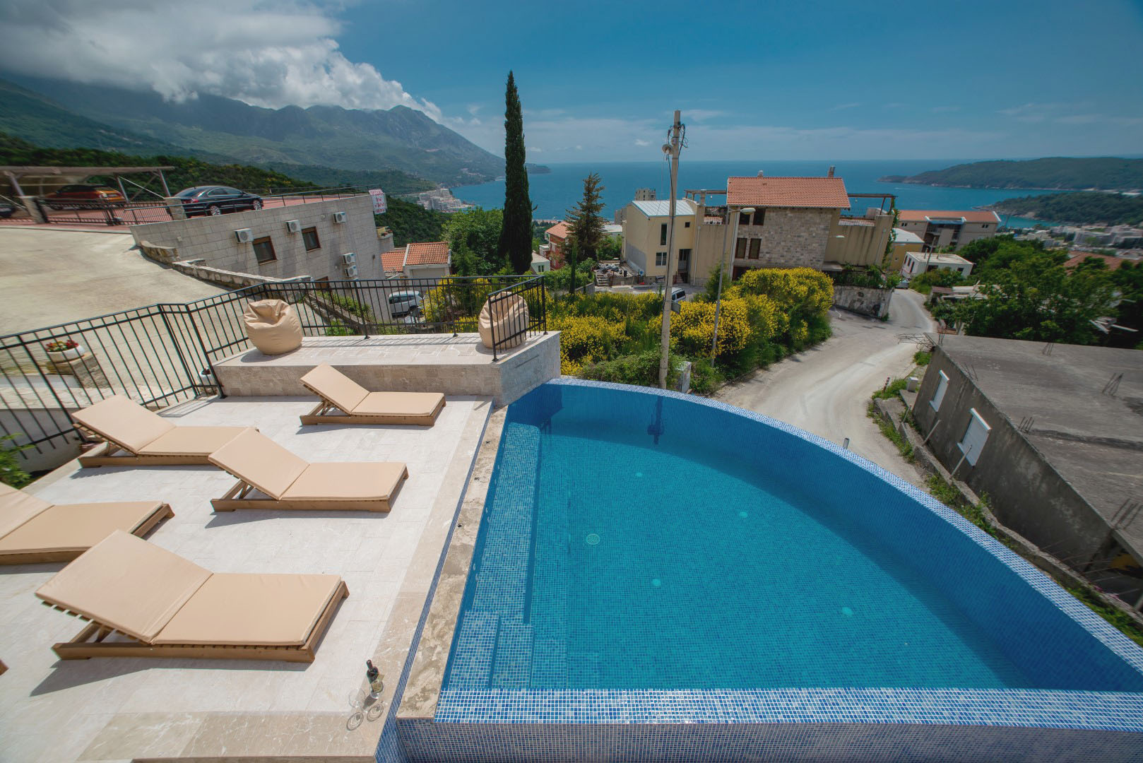 Offener Pool mit Blick auf das Meer und die Berge in einer Villa in Bečići, Montenegro, mit Ruhebereich und Sonnenliegen auf der Terrasse.