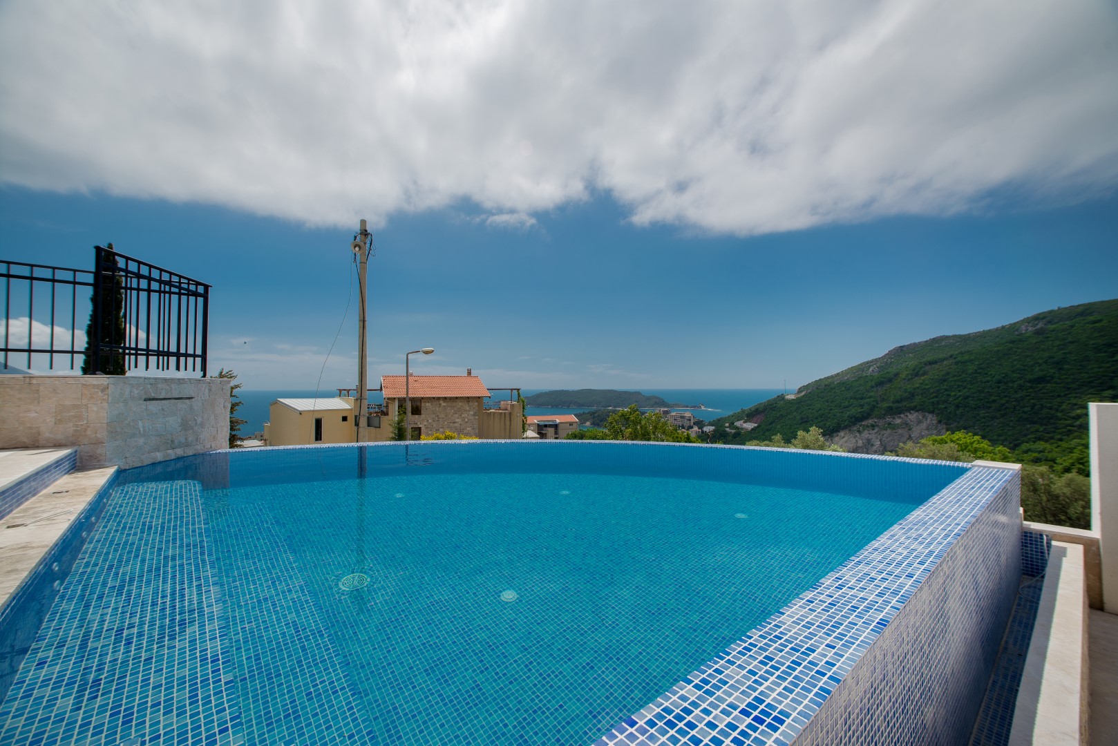 Offener Pool mit Panoramablick auf das Meer und die Berge in einer Villa in Bečići, Montenegro. Poolverkleidung aus blauer Mosaikfliese.