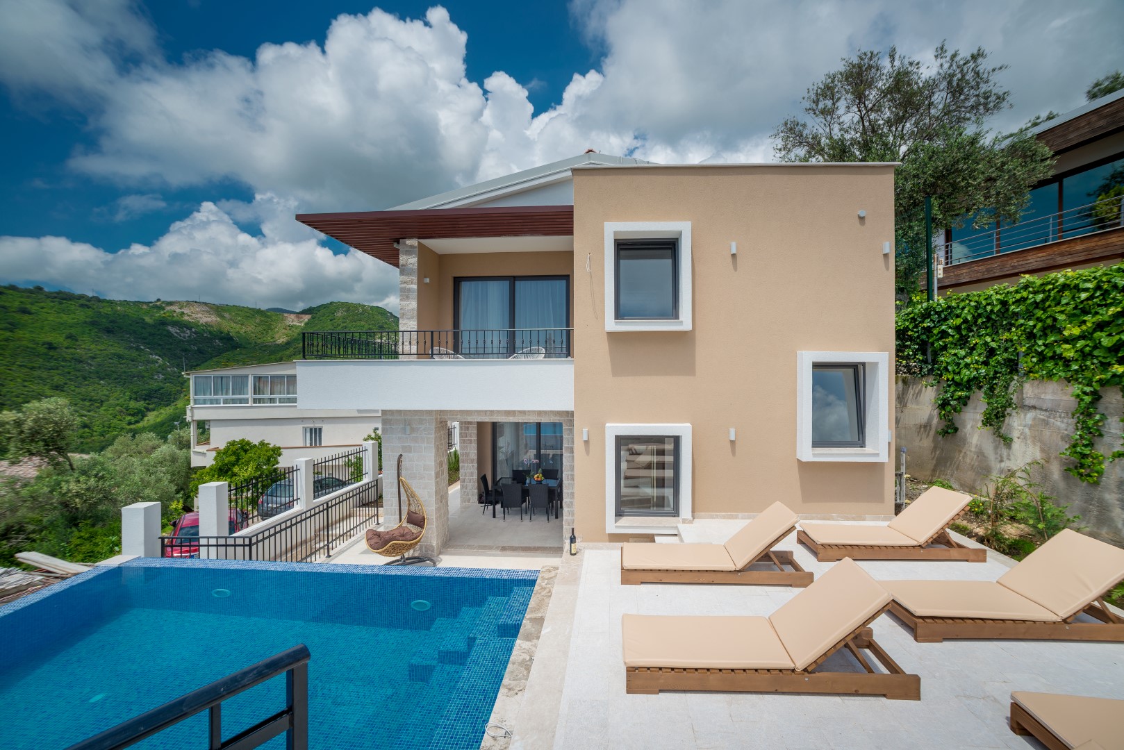 Moderne Villa in Bečići, Montenegro: Pool, Terrasse mit Liegestühlen, Bergblick und stilvolle Fassadengestaltung.