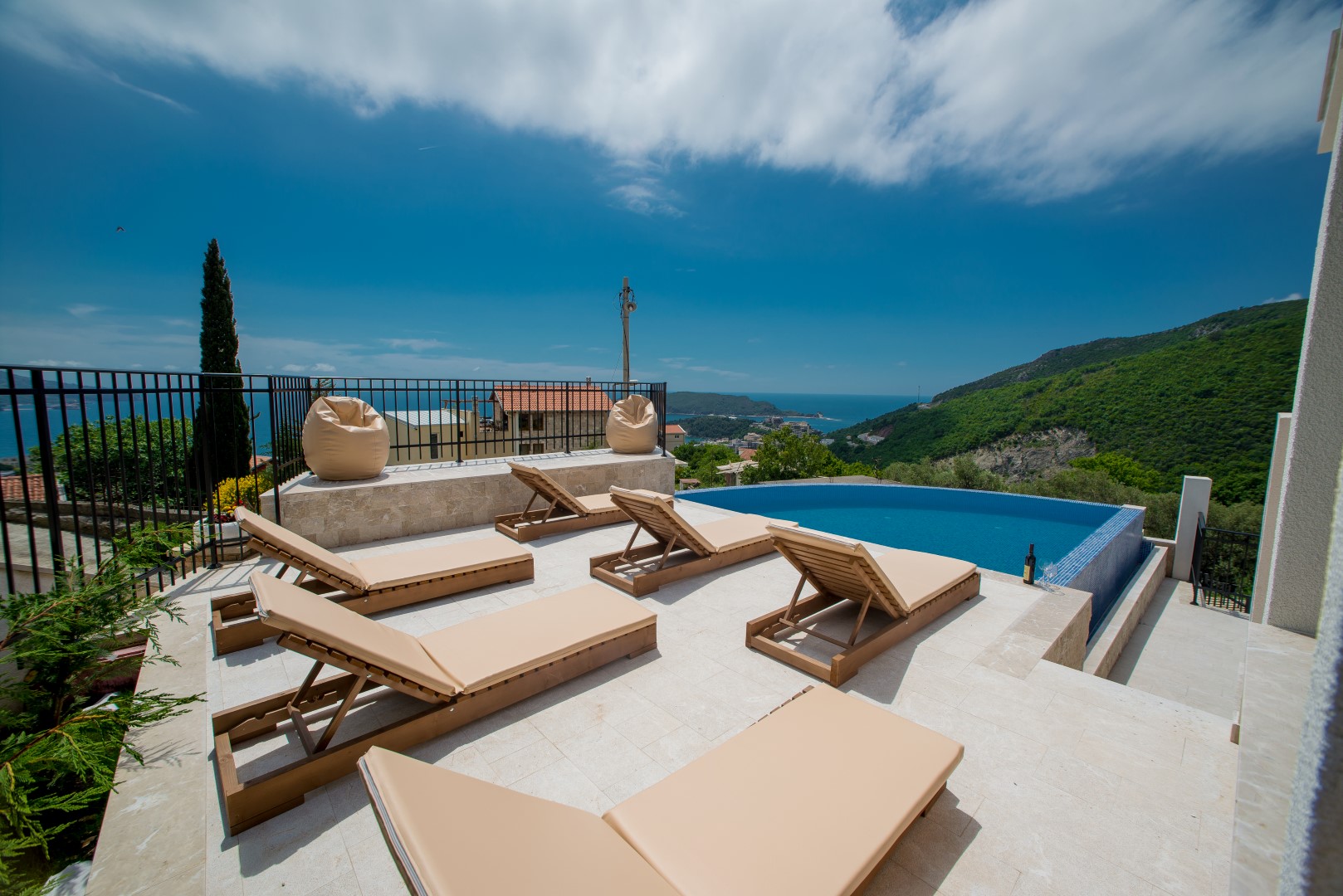 Terrasse mit Pool und Liegestühlen in einer Villa in Bečići, Montenegro, mit Panoramablick auf das Meer und die Berge.