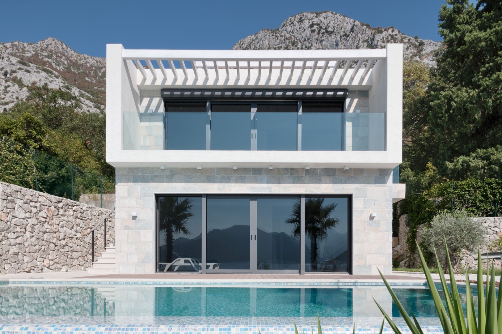 Karadağ, Strp’te modern villa: taş cepheli dış cephe, panoramik pencereler, balkon ve evin yanında özel havuz.