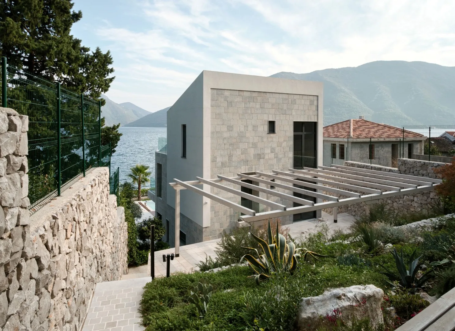 Современная вилла из камня с террасой и видом на море в поселке Стрп, Черногория, окруженная ландшафтным садом.