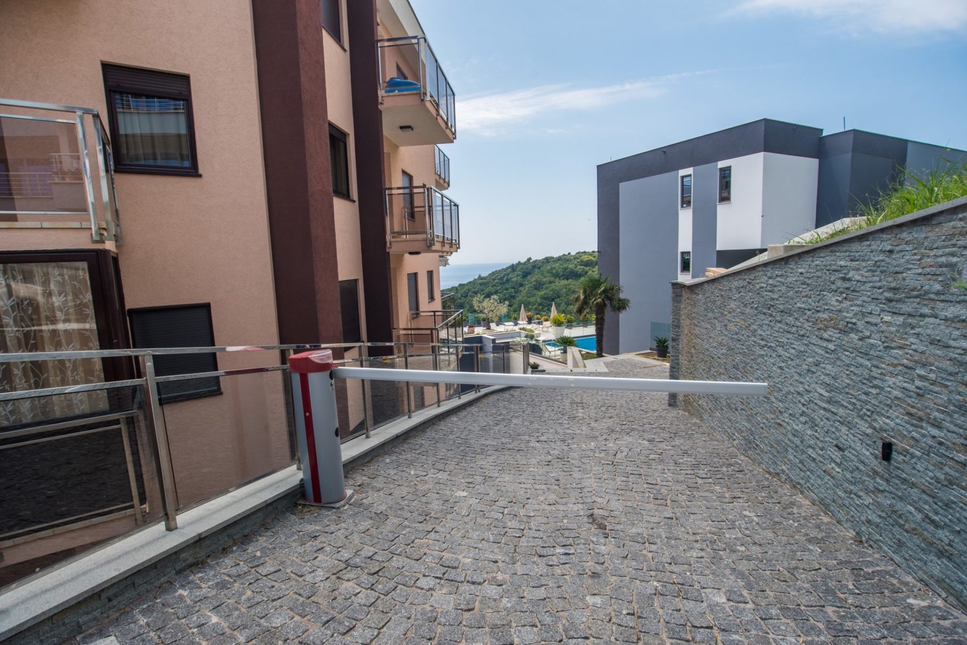 Einfahrt mit Schranke auf das abgeschlossene Villengelände in Budva, Montenegro, mit Meer- und Poolblick.