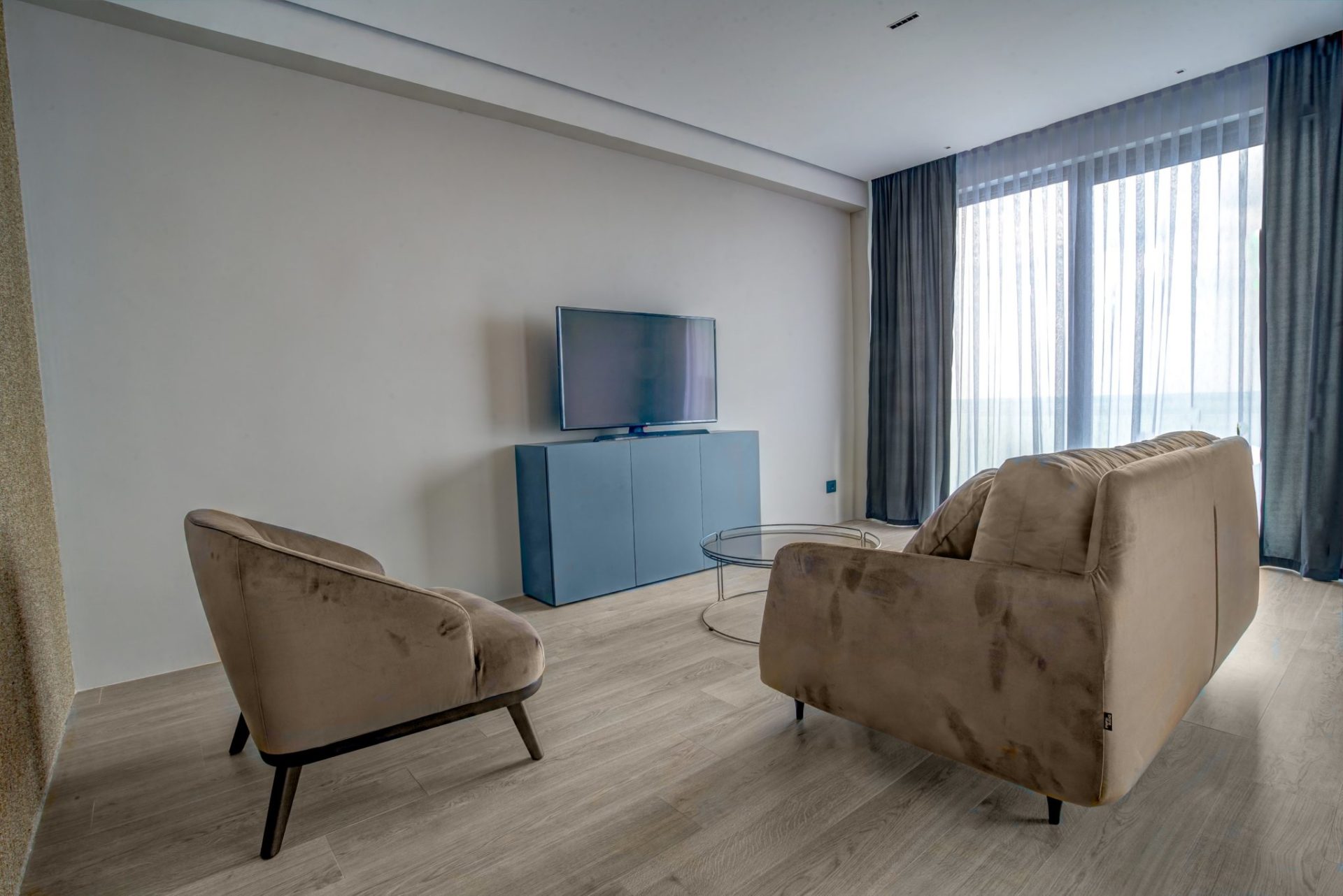 Modernes Wohnzimmer mit beigem Sofa, Sessel und TV-Bereich in einer Villa in Budva, Montenegro. Helles Interieur mit Panorama.