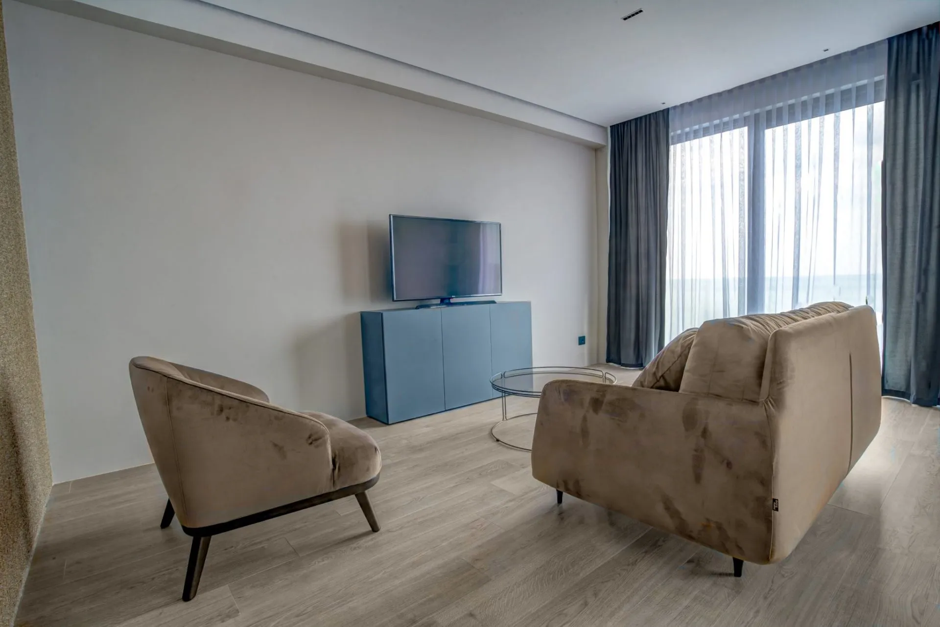 Modernes Wohnzimmer mit beigem Sofa, Sessel und TV-Bereich in einer Villa in Budva, Montenegro. Helles Interieur mit Panorama.