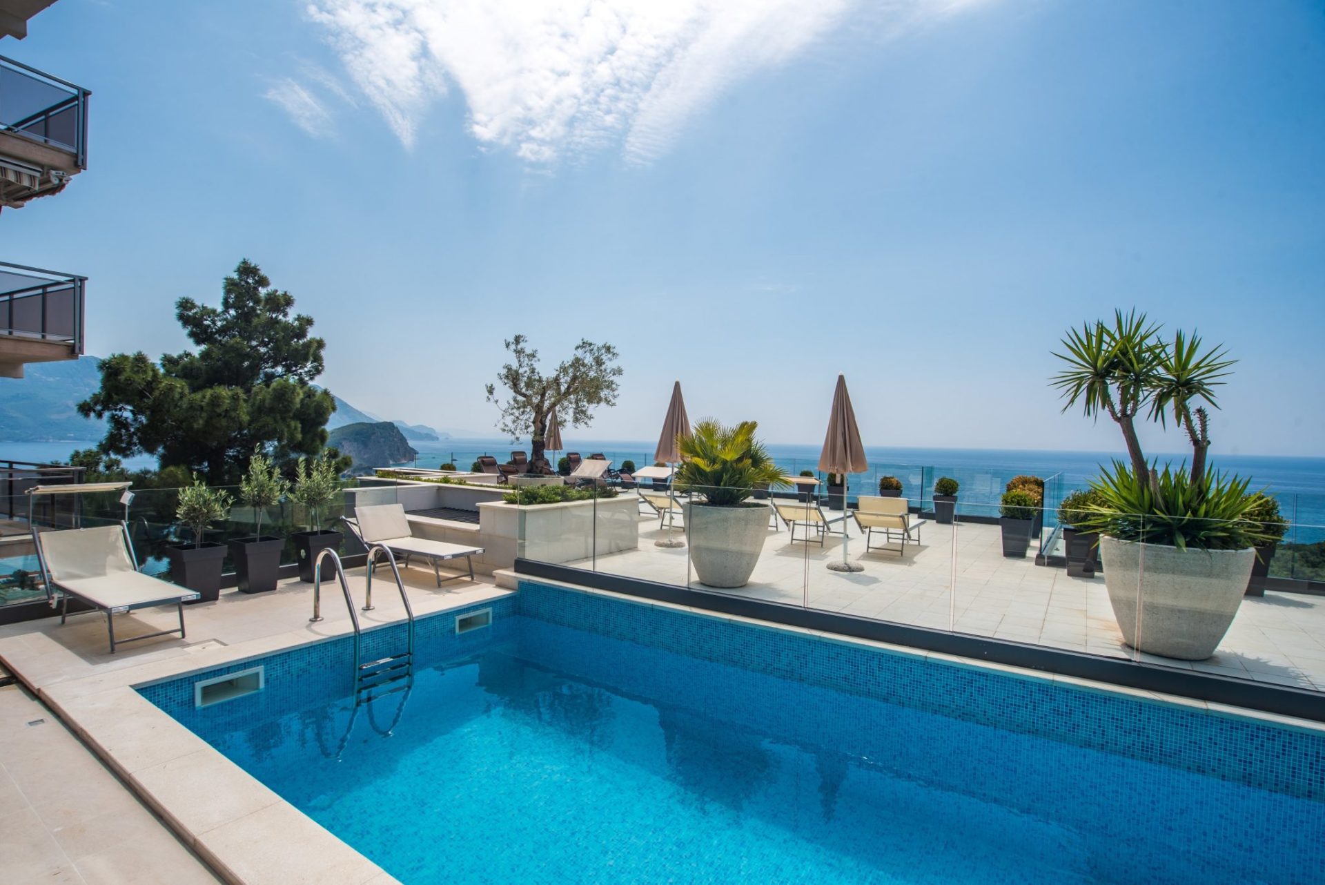 Offener Pool auf der Terrasse einer Villa in Budva, Montenegro, mit Liegestühlen, Pflanzen und Panoramablick auf die Adria.