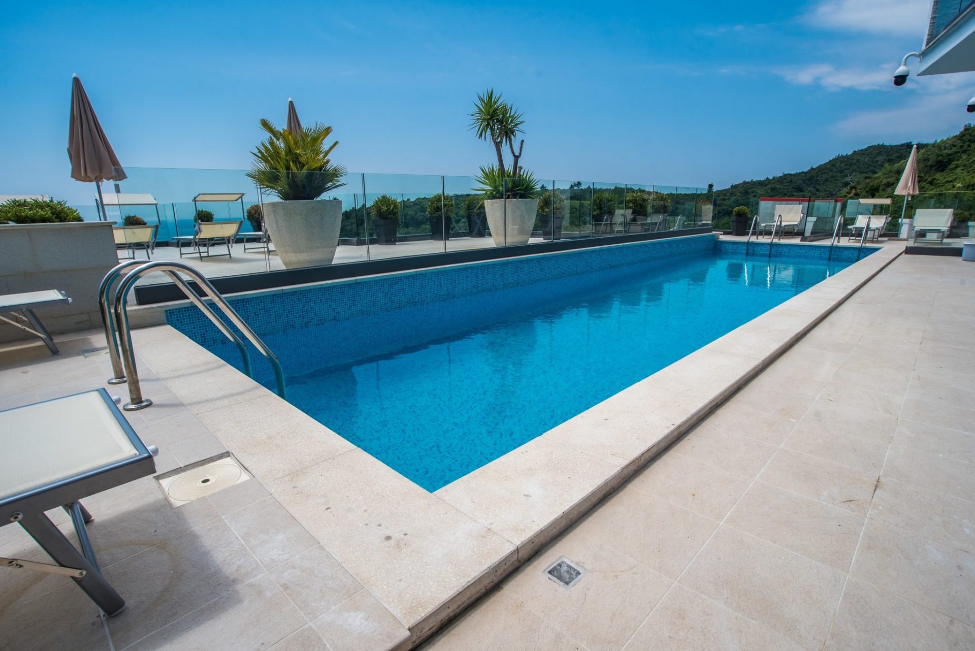 Offener Pool auf der Terrasse einer Villa in Budva, Montenegro, mit Liegestühlen, Glasgeländer und Bergblick.