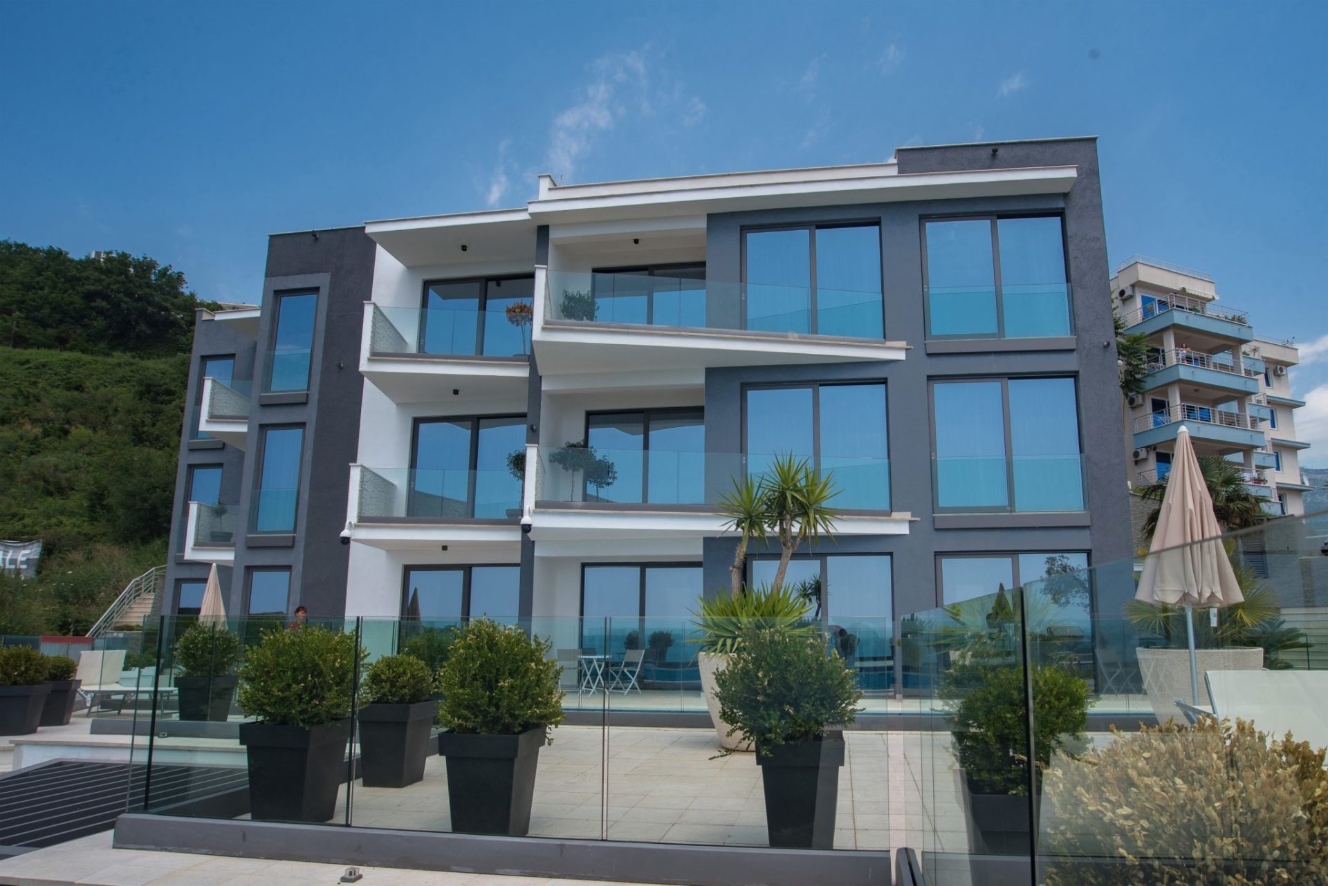 Moderne Villa in Budva, Montenegro: Fassade mit Panoramafenstern, Glasbalkonen und einer Terrasse mit Pflanzen.