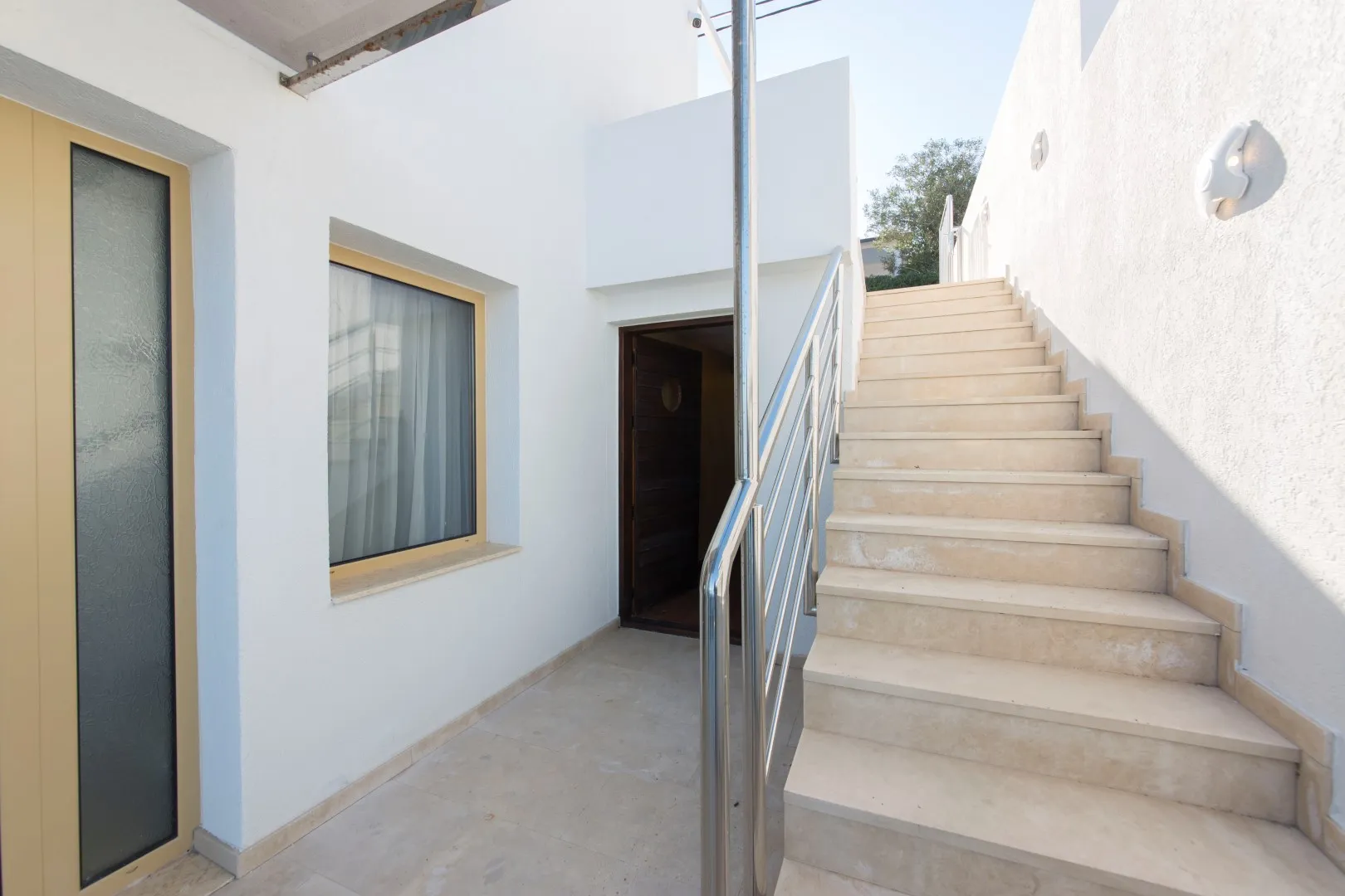 Entrance to a villa in Krašići, Montenegro: white finish, stone staircase with metal railings, and an entrance door.