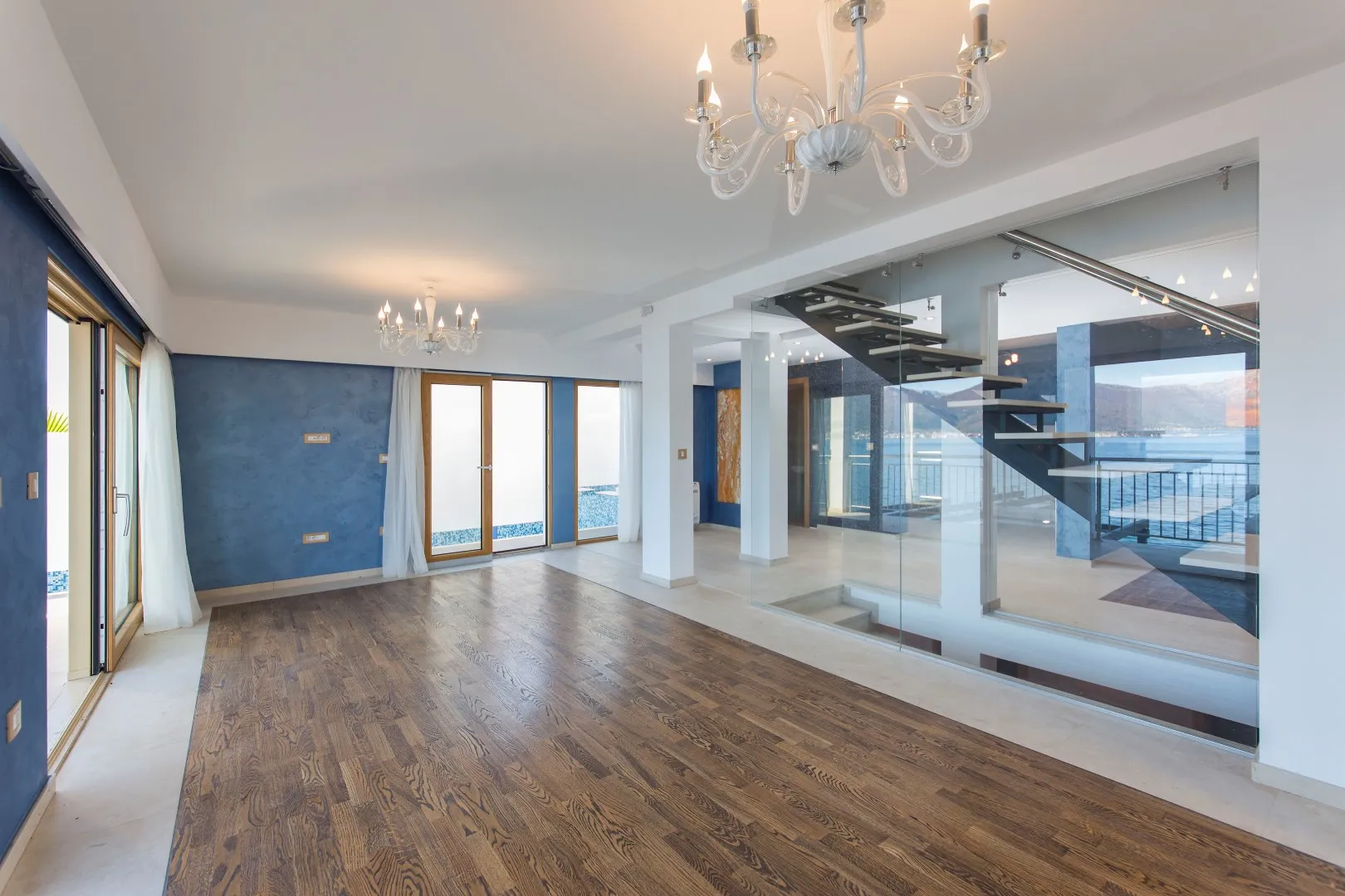 Spacious villa living room in Krašići, Montenegro: wooden floor, glass staircase, and panoramic sea view.