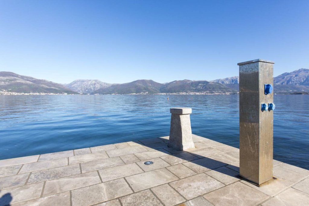 Stone pier with a yacht mooring post and panoramic views of the sea and mountains in the village of Krašići, Montenegro.