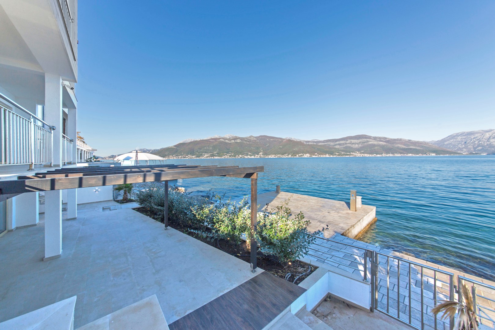 Villa terrace in Krašići, Montenegro, with a private pier, sea and mountain views, modern finishes, and a canopy.