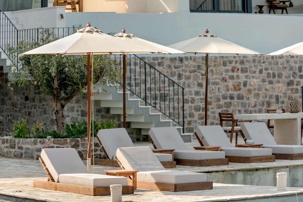 Poolbereich einer Villa in Luštica, Montenegro: Liegestühle, Sonnenschirme und Steinverkleidung der Fassade.