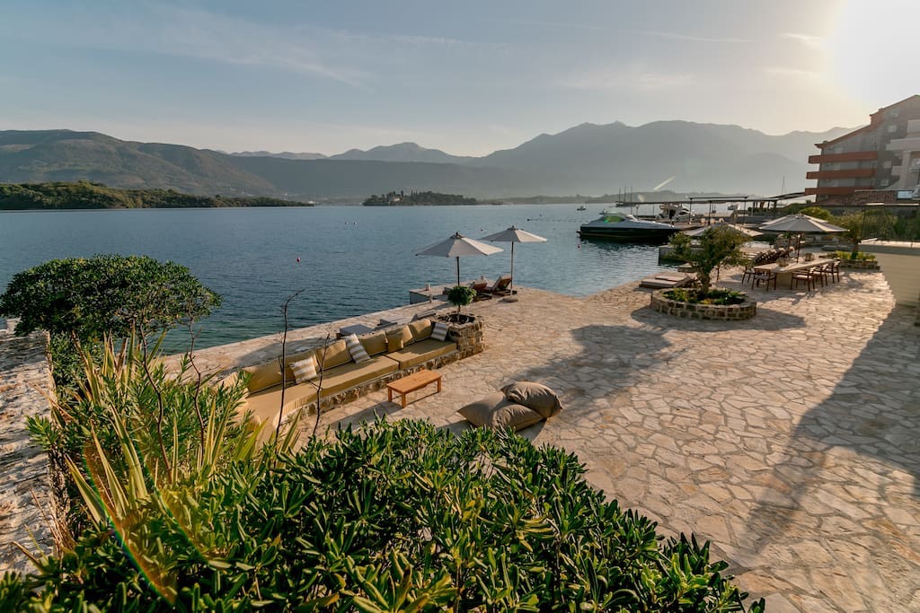 Terrasse der Villa in erster Meereslinie in Luštica, Montenegro: Steinverkleidung, Loungebereich mit Sofas und Blick auf das Meer und die Berge.