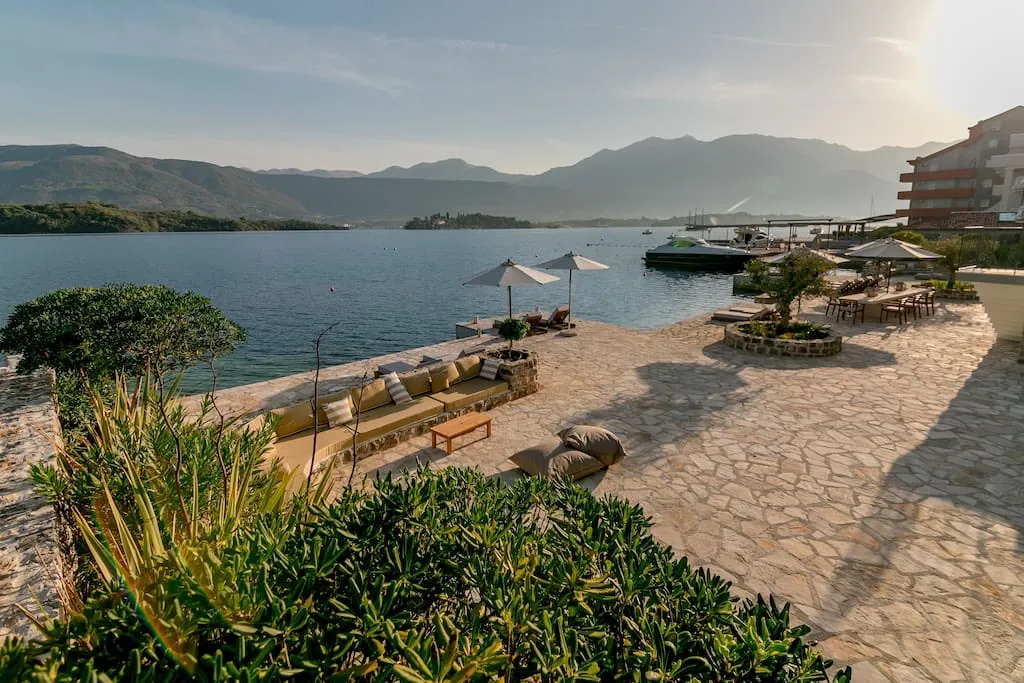 Terrasse der Villa in erster Meereslinie in Luštica, Montenegro: Steinverkleidung, Loungebereich mit Sofas und Blick auf das Meer und die Berge.