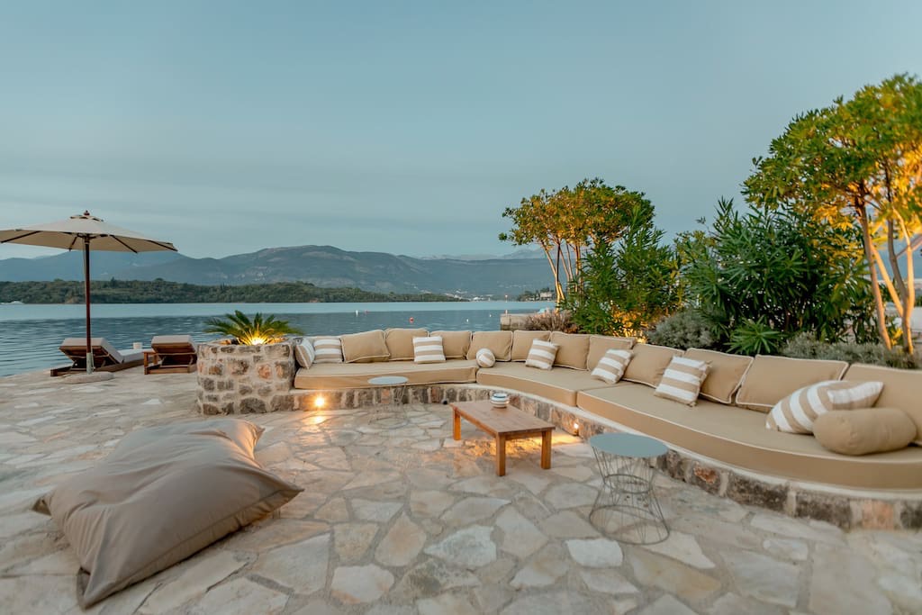 Terrasse der Villa in erster Meereslinie in Luštica, Montenegro: Steinverkleidung, weiches Sofa, Blick auf das Meer und die Berge.