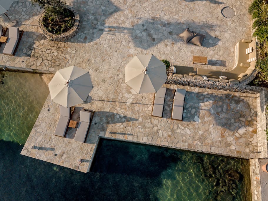 Terrasse der Villa in erster Meereslinie in Luštica, Montenegro: Pool, Liegen, Sonnenschirme und Lounge-Bereich mit Steinverkleidung.